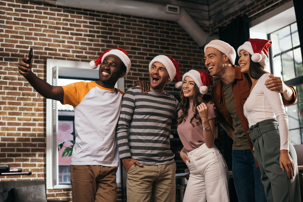 onnellinen monikulttuurinen liikemiehet santa hatut ottaen selfie älypuhelimeen toimistossa
 - Valokuva, kuva