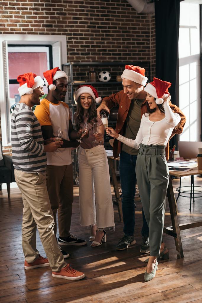 šťastný multikulturní podnikatelé v Santa klobouky cinkání sklenice šampaňského v kanceláři - Fotografie, Obrázek