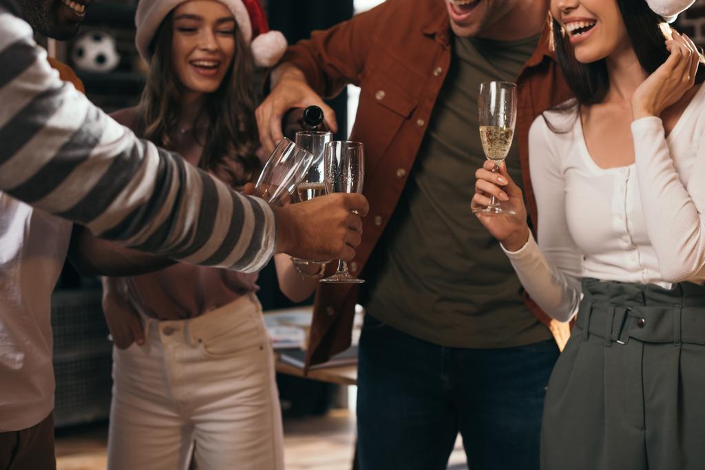 částečný pohled na obchodníka nalévání šampaňského v brýlích šťastných kolegů v Santa Kloboucích - Fotografie, Obrázek