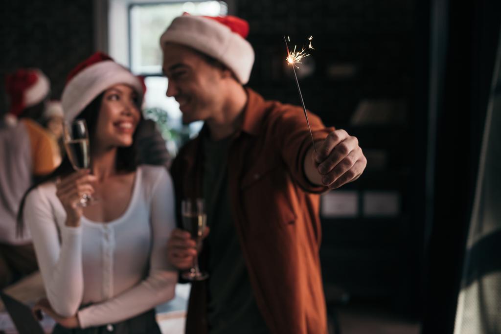 selective focus of young businessman holding sparkler near attractive, smiling colleague  - Photo, Image