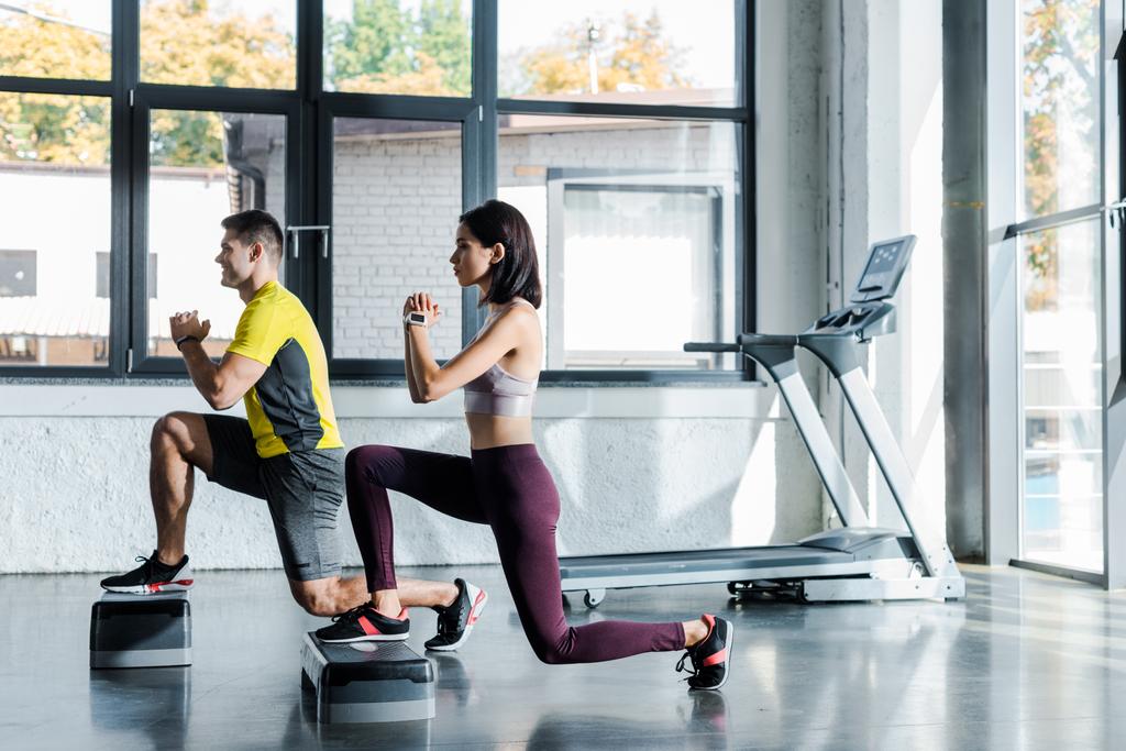 side view of handsome sportsman and sportswoman doing lunges on step platforms in sports center - Photo, Image