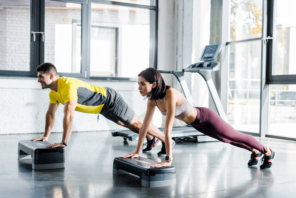 handsome sportsman and sportswoman doing plank on step platforms in sports center - Photo, Image