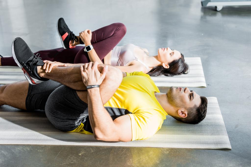 sportman en sportvrouw stretching op fitnessmatten in sportcentrum - Foto, afbeelding