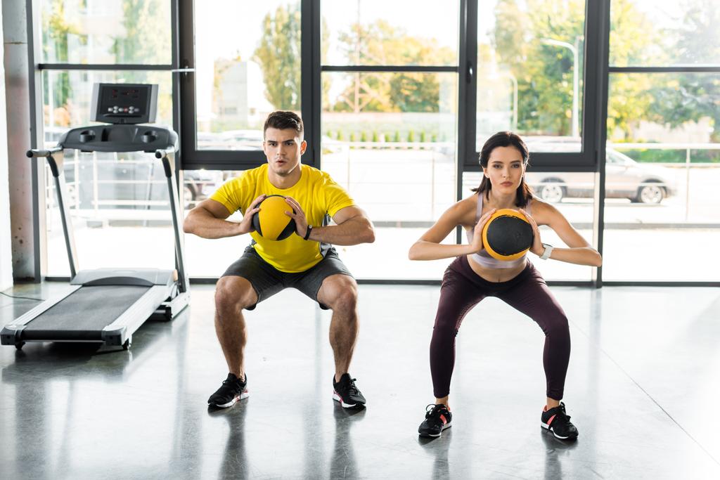 sportsman and sportswoman doing squat with balls in sports center - Photo, Image