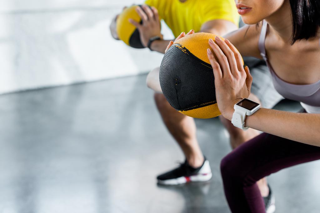cropped view of sportsman and sportswoman doing squat with balls in sports center - Photo, Image