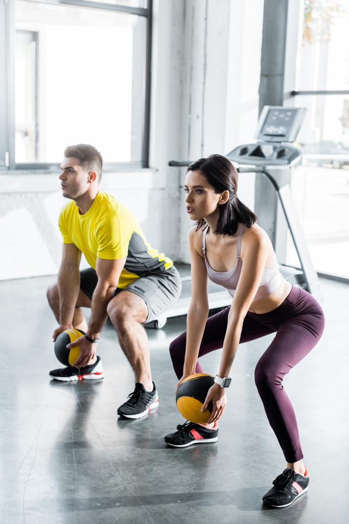 sportsman and sportswoman doing squat with balls in sports center - Photo, Image