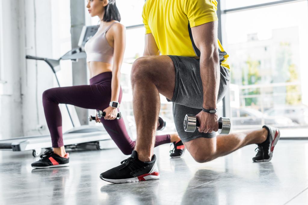 cropped view of sportsman and sportswoman doing lunges with dumbbells in sports center - Photo, Image