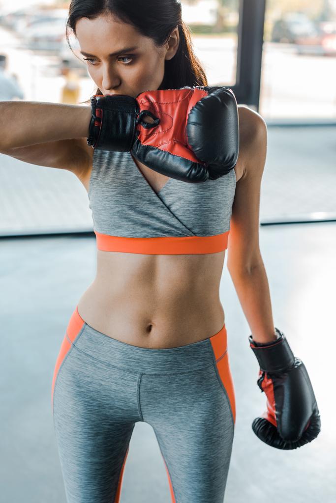 Αθλητική γυναίκα σε γάντια πυγμαχίας κοιτάζοντας κάτω στο αθλητικό κέντρο  - Φωτογραφία, εικόνα