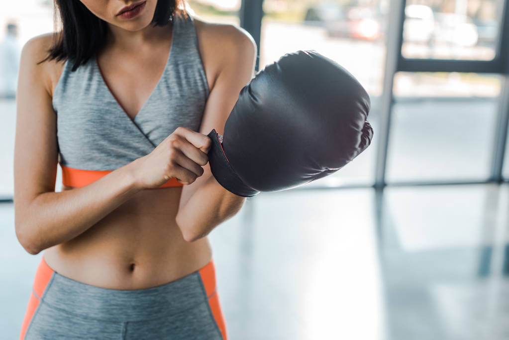 スポーツセンターでボクシンググローブを身に着けているスポーツ女性のクロップドビュー  - 写真・画像