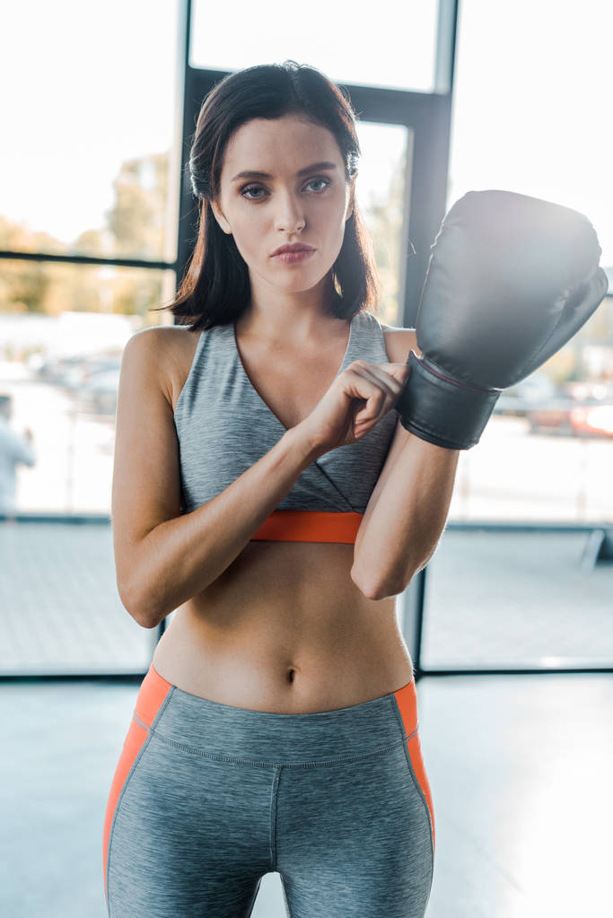 sportvrouw draagt bokshandschoen en kijkt naar camera in sportcentrum  - Foto, afbeelding