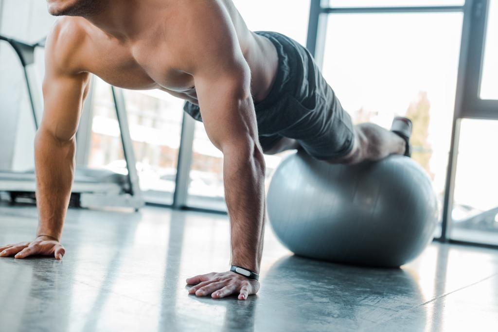 cropped view of handsome sportsman doing plank on fitness ball in sports center  - Photo, Image