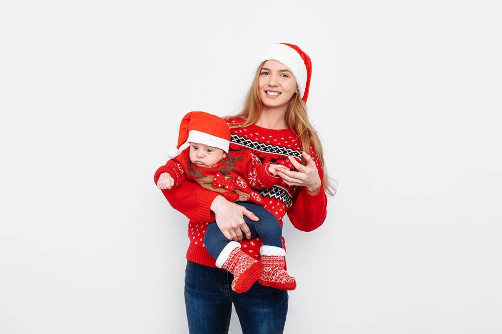 Giovane madre in cappello di Babbo Natale con bambino in costume da Babbo Natale in piedi su sfondo bianco
 - Foto, immagini