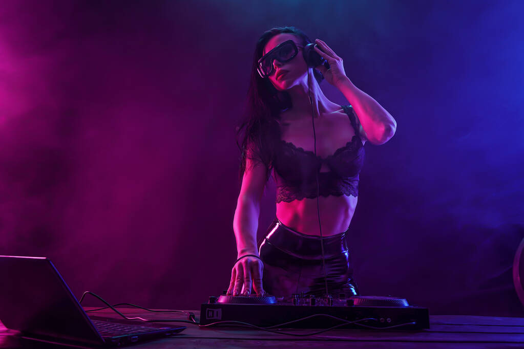 Νέα σέξι γυναίκα dj παίζει μουσική. Ακουστικά και dj mixer στο τραπέζι. - Φωτογραφία, εικόνα