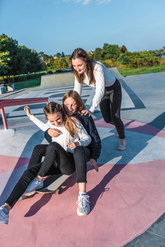 Schülerinnen Teenager Mädchen, 3 Freundinnen fahren Skateboard, herbstliche warme Pullover haben Spaß, glücklich Spaß haben, spielen, nach der Schule entspannen, Emotionen der Freude und Freude am Vergnügen. im Sommer Stadtnatur - Foto, Bild