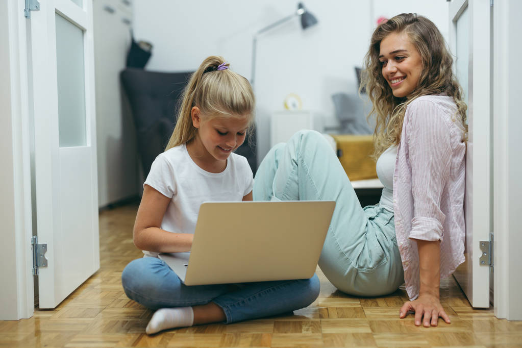 Mutter und Tochter benutzen Laptop zu Hause auf dem Fußboden - Foto, Bild