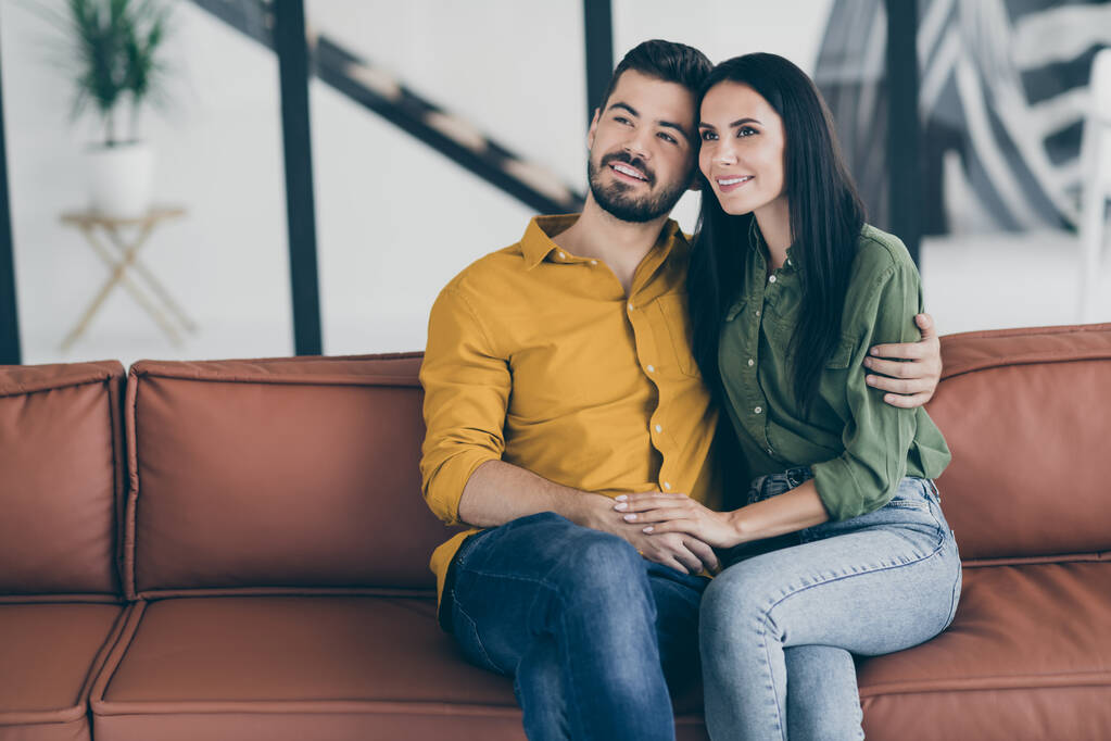 Фото парня и его жены, переезжающей в новый загородный дом, в то время как женатые люди, обнимающиеся, держась за руки, сидят на диване в современной квартире
 - Фото, изображение