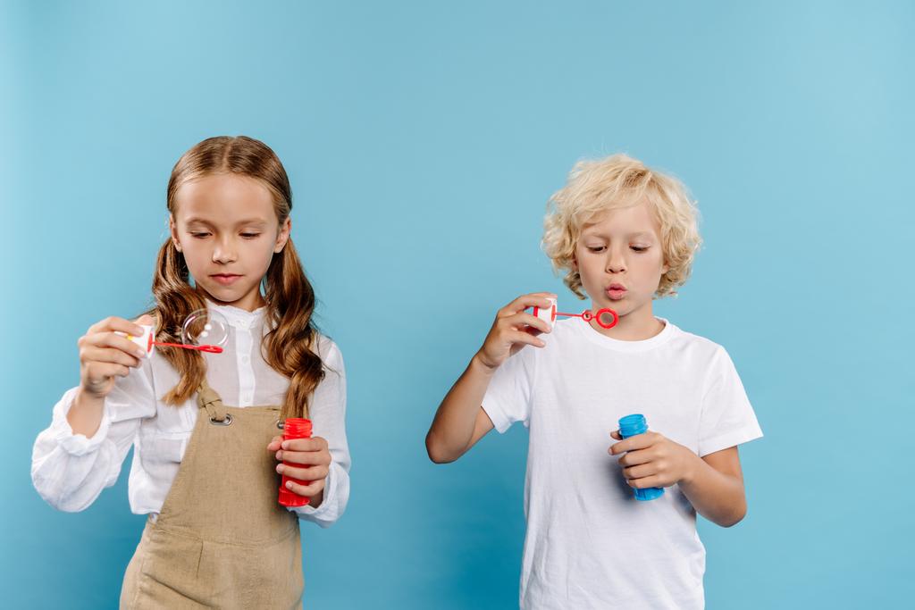 roztomilé děti drží láhve a foukání mýdlo bubliny na modrém pozadí  - Fotografie, Obrázek