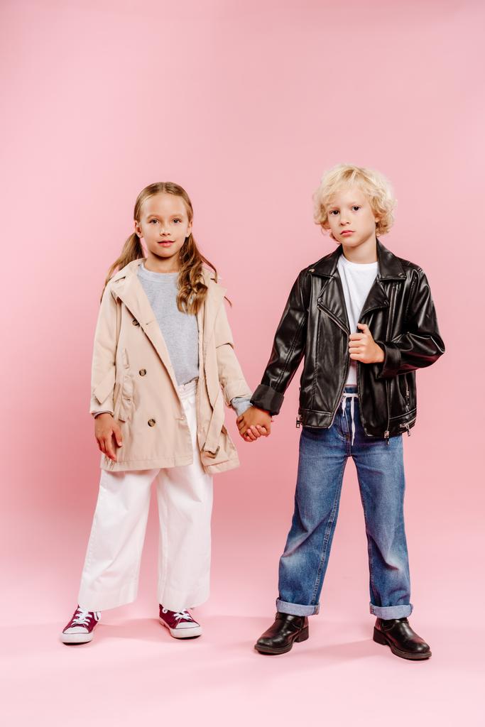 crianças de casaco e jaqueta de couro de mãos dadas e olhando para a câmera no fundo rosa
  - Foto, Imagem