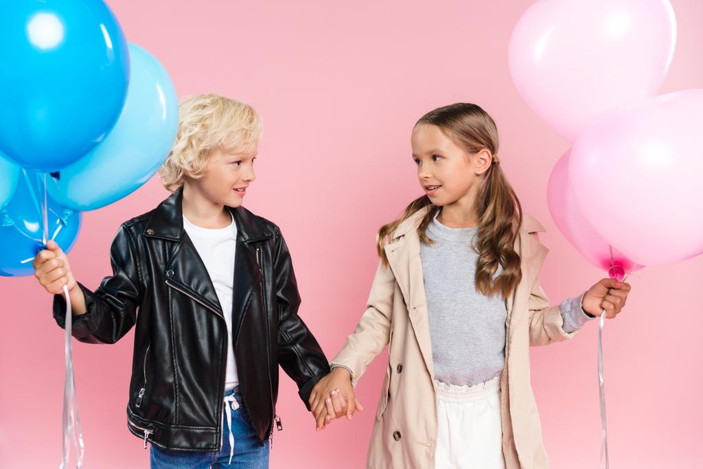 niños sonrientes sosteniendo globos y tomándose de las manos sobre fondo rosa
  - Foto, imagen