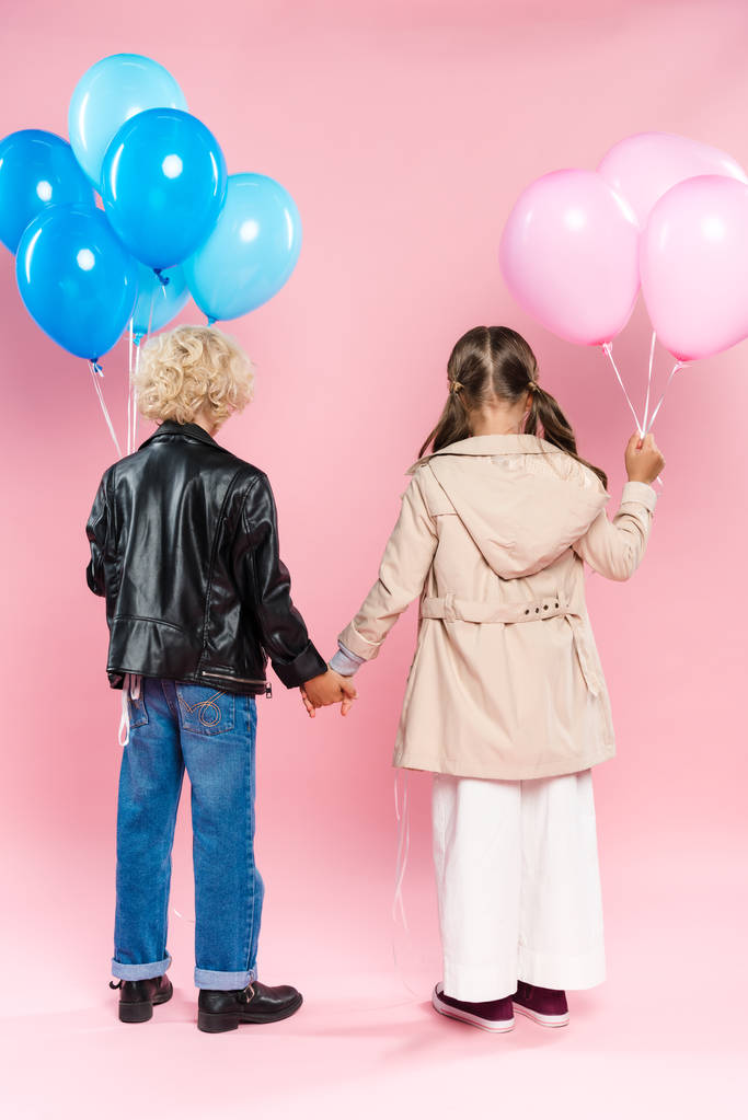visão traseira de crianças segurando balões e de mãos dadas no fundo rosa
  - Foto, Imagem