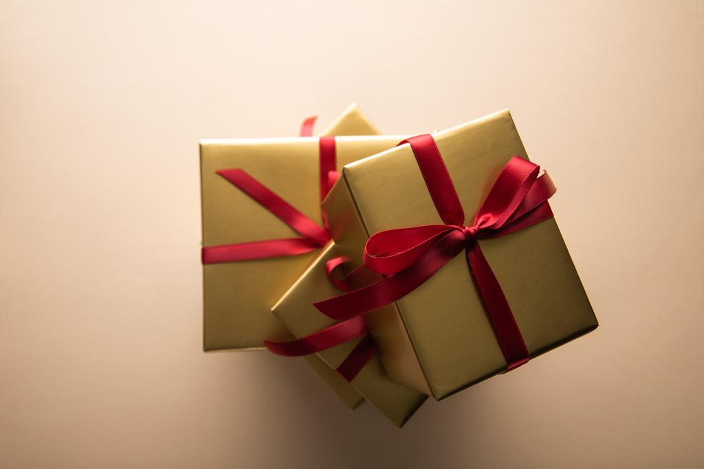 vue du dessus des boîtes-cadeaux dorées avec rubans rouges et noeuds sur fond beige
 - Photo, image