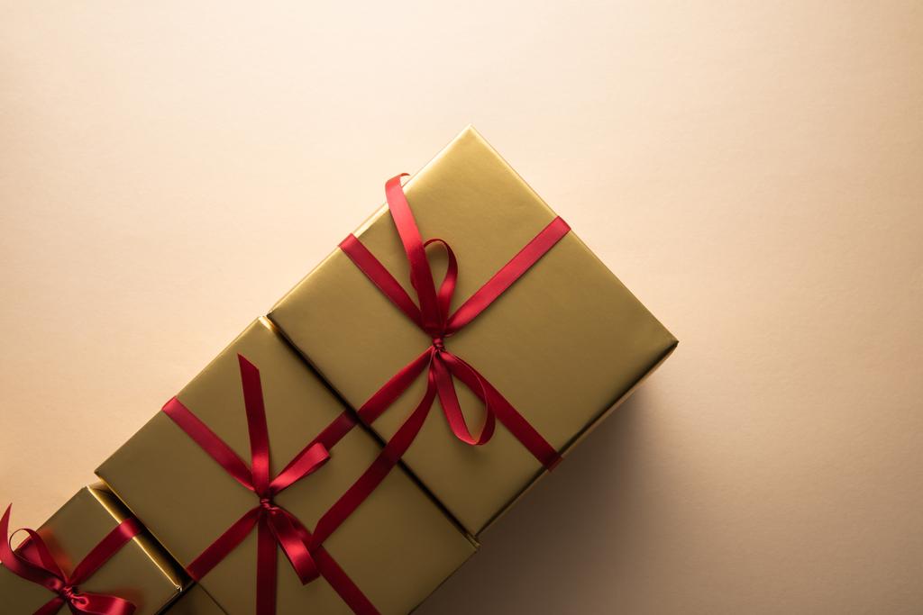 πάνω όψη από χρυσά κουτιά δώρου με κόκκινες κορδέλες και φιόγκους σε μπεζ φόντο - Φωτογραφία, εικόνα