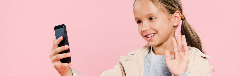 plano panorámico de niño sonriente y lindo ondeando durante el chat de vídeo aislado en rosa
 - Foto, Imagen