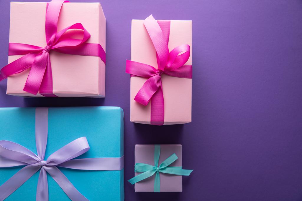 bovenaanzicht van kleurrijke geschenkdozen met linten en strikken op paarse achtergrond met kopieerruimte - Foto, afbeelding