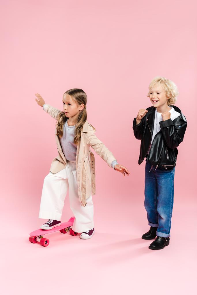 Kind reitet Penny Board und Junge zeigt Ja-Geste auf rosa Hintergrund  - Foto, Bild