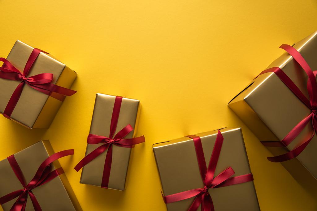 πάνω όψη από χρυσά κουτιά δώρων με κόκκινες κορδέλες σε κίτρινο φόντο με αντίγραφο χώρου - Φωτογραφία, εικόνα