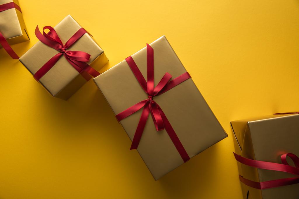 πάνω όψη από χρυσά κουτιά δώρου με κόκκινες κορδέλες σε κίτρινο φόντο - Φωτογραφία, εικόνα