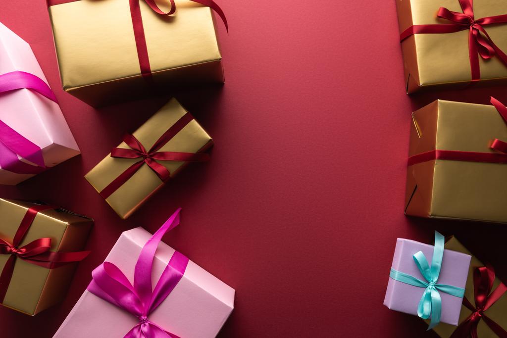 Draufsicht auf bunte Geschenkboxen mit Bändern auf rotem Hintergrund mit Kopierraum - Foto, Bild