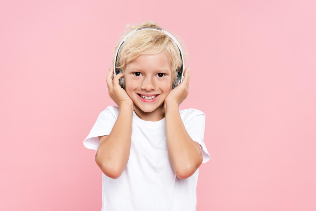 niño sonriente con auriculares escuchando música aislada en rosa
 - Foto, Imagen