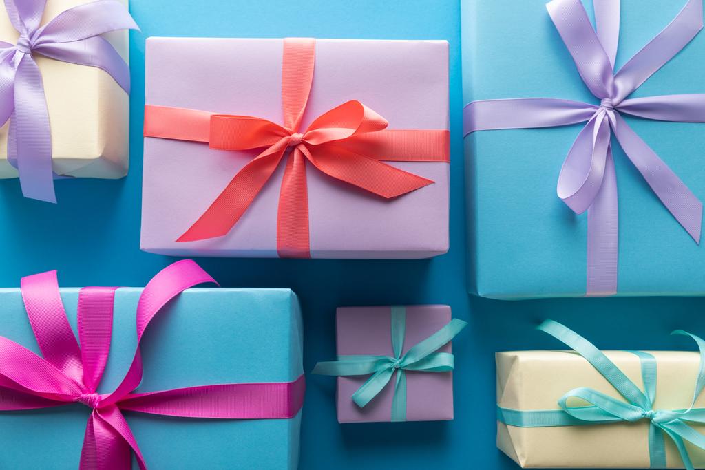 επίπεδο θέσει με πολύχρωμα κουτιά δώρο με κορδέλες σε μπλε φόντο - Φωτογραφία, εικόνα