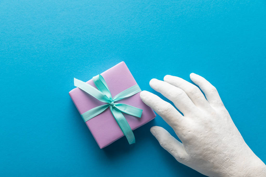 обрізаний вид пофарбованої руки біля фіолетової подарункової коробки на синьому фоні
 - Фото, зображення