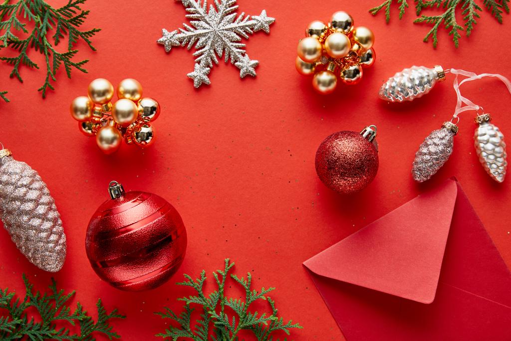 horní pohled na lesklé vánoční dekorace, obálka a thuja na červeném pozadí - Fotografie, Obrázek