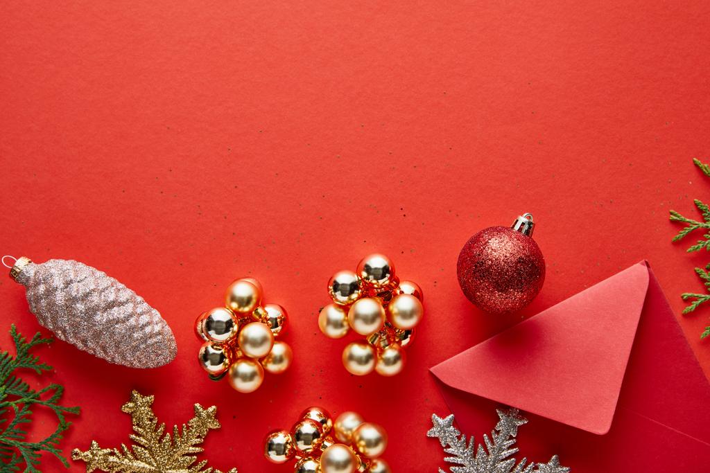 top view of shiny Christmas decoration, envelope and thuja on red background with copy space - Photo, Image
