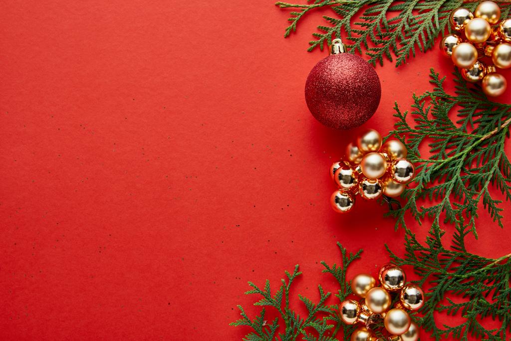 κορυφαία άποψη του γυαλιστερού χριστουγεννιάτικη διακόσμηση και πράσινο thuja σε κόκκινο φόντο με αντίγραφο χώρου - Φωτογραφία, εικόνα