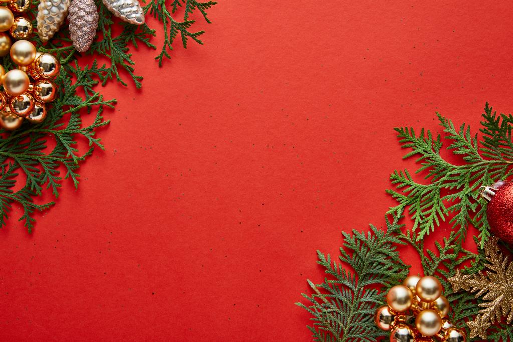 コピースペースと赤の背景に緑のthujaの枝の光沢のあるクリスマスの装飾のトップビュー - 写真・画像