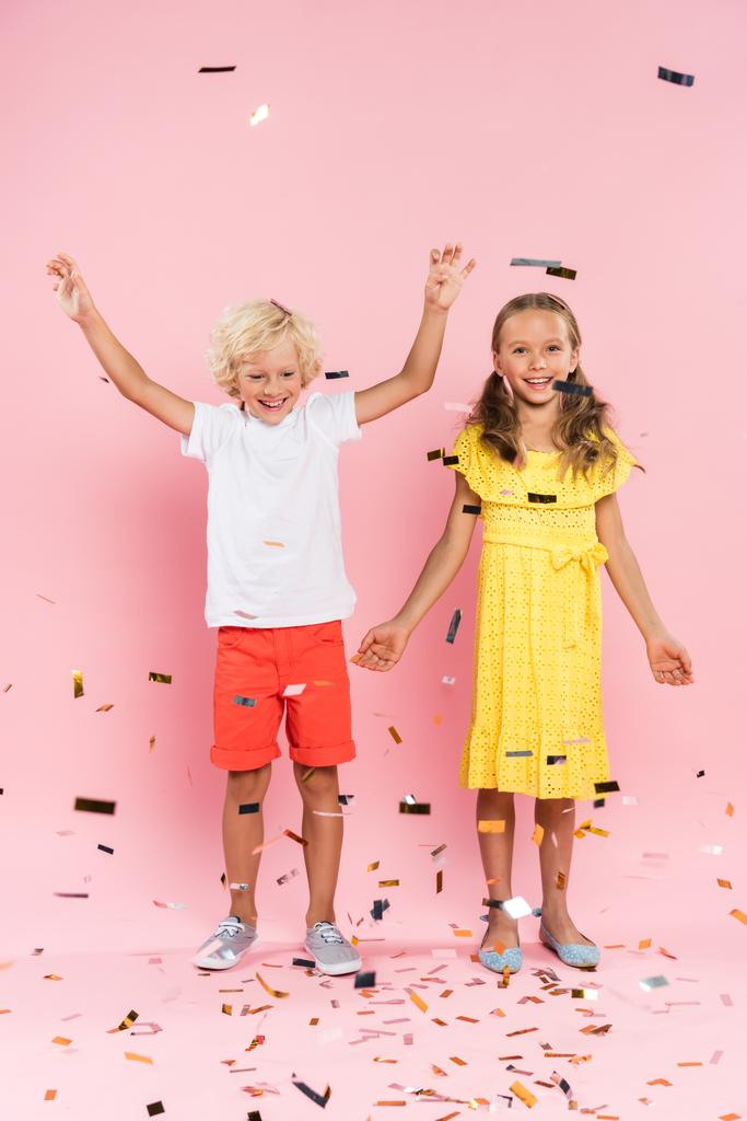 smiling kids with outstretched hands near falling confetti on pink background  - Photo, Image