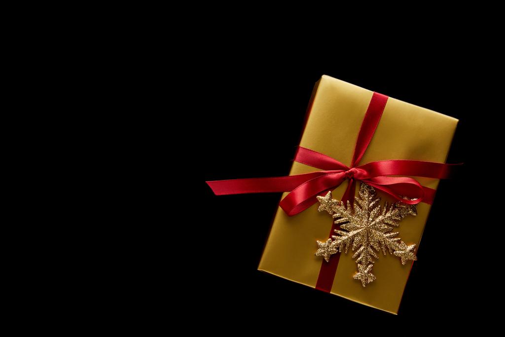 felső nézet fényes arany karácsonyi ajándék piros szalaggal és hópihe elszigetelt fekete - Fotó, kép
