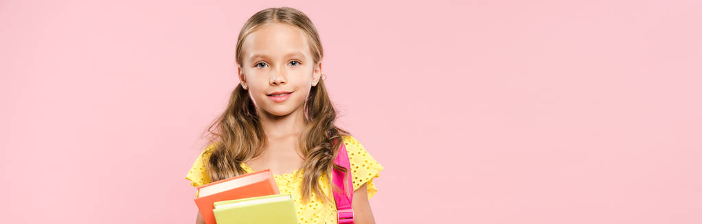 plano panorámico de colegiala sonriente con mochila sosteniendo libros aislados en rosa
 - Foto, imagen