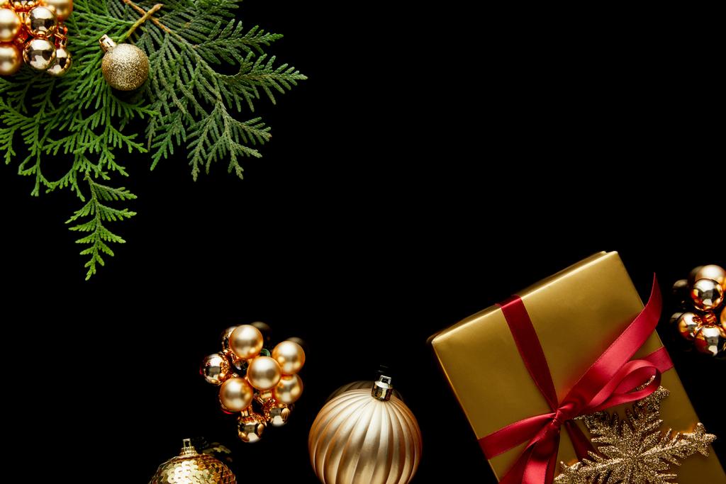widok z góry błyszczące złote dekoracje świąteczne, zielone gałęzie thuja i pudełko prezentów izolowane na czarno - Zdjęcie, obraz