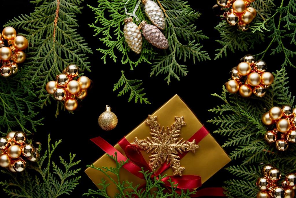 Parlak altın Noel süslemeleri, yeşil thuja dalları ve siyah üzerine izole edilmiş hediye kutusu. - Fotoğraf, Görsel