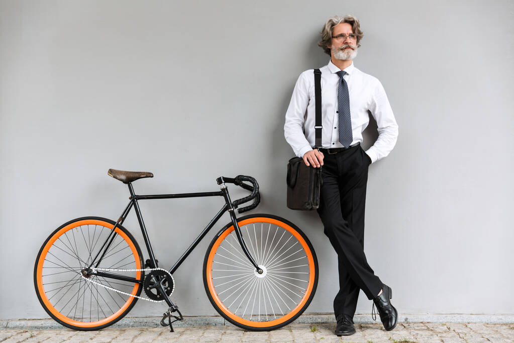 Foto de um velho empresário sério de pé com bicicleta
 - Foto, Imagem