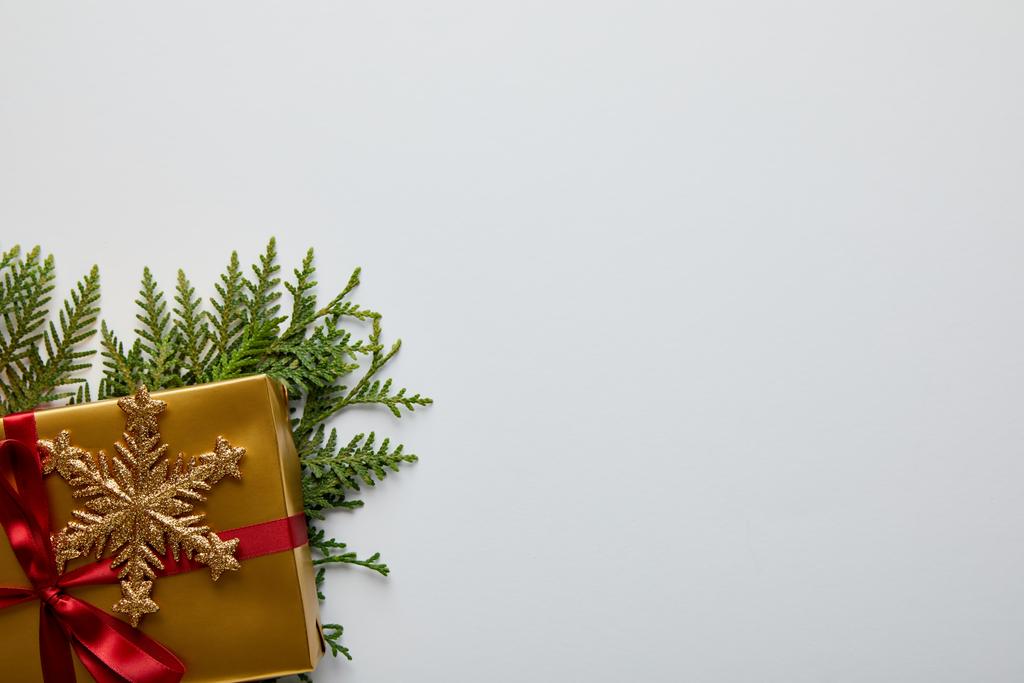верхний вид блестящей золотой снежинки, зеленые ветки туи и подарочная коробка изолированы на белом с копировальным пространством
 - Фото, изображение