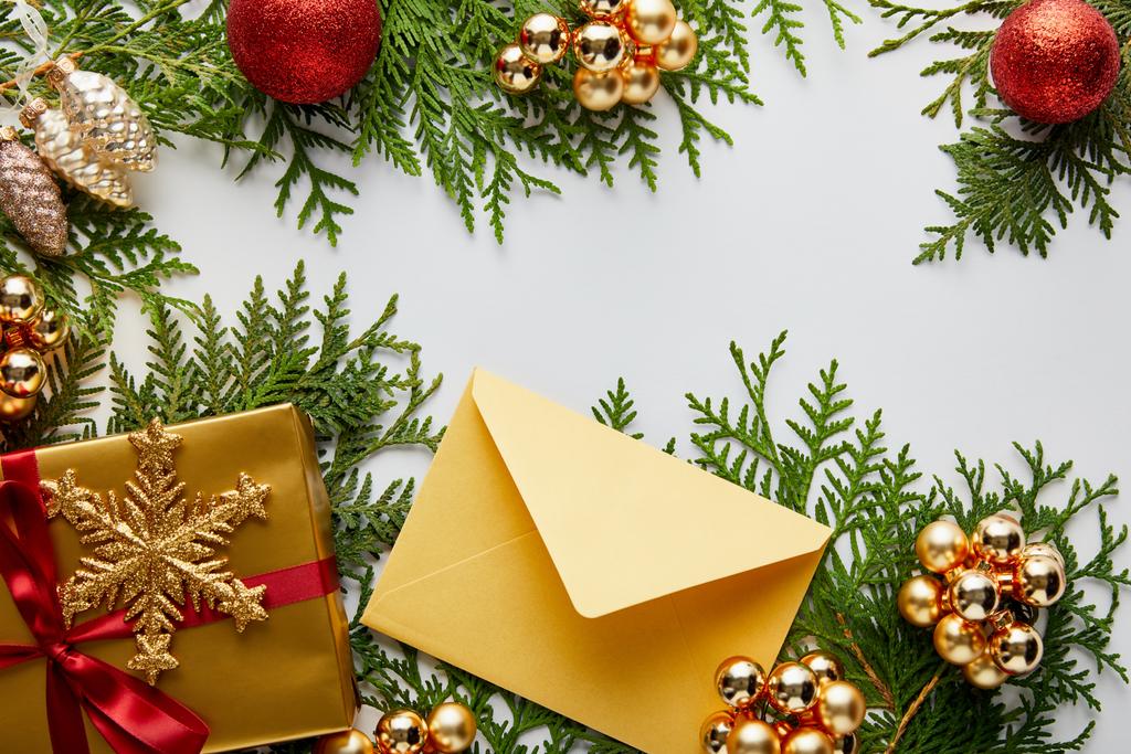 верхний вид блестящего золотистого рождественского украшения, подарок и конверт на зеленые ветви туи изолированы на белом
 - Фото, изображение