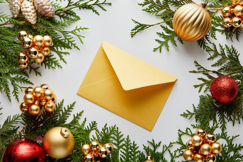 Yeşil thuja dalları üzerindeki parlak altın ve kırmızı Noel süslemesi ve beyaz üzerine izole edilmiş bir zarf. - Fotoğraf, Görsel