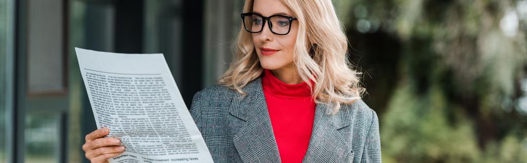 Paltolu ve gözlüklü çekici iş kadınının gazete okuduğu panoramik bir fotoğraf.  - Fotoğraf, Görsel