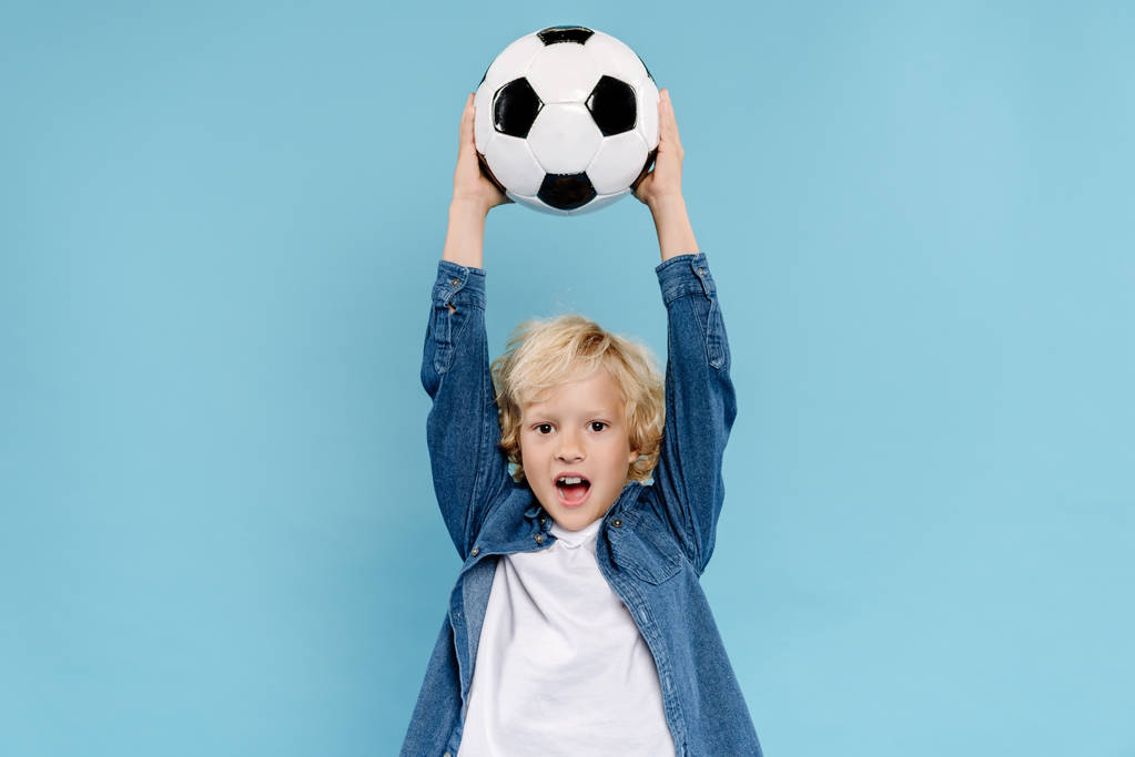 милый ребенок держит футбол и кричит изолированы на синий
  - Фото, изображение